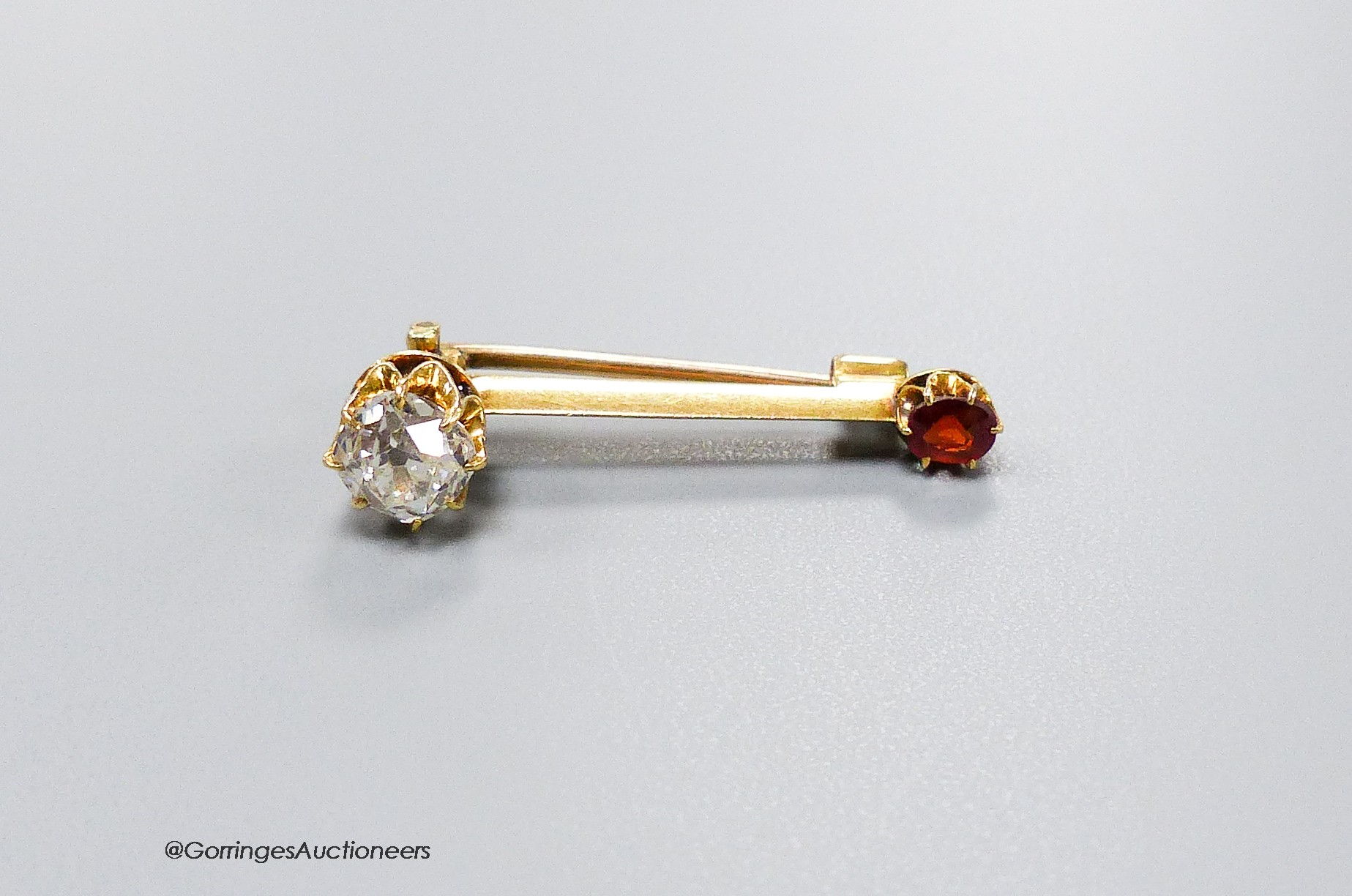 A small yellow metal, cushion cut diamond and garnet? set two stone bar brooch, 30mm, gross weight 3.1 grams